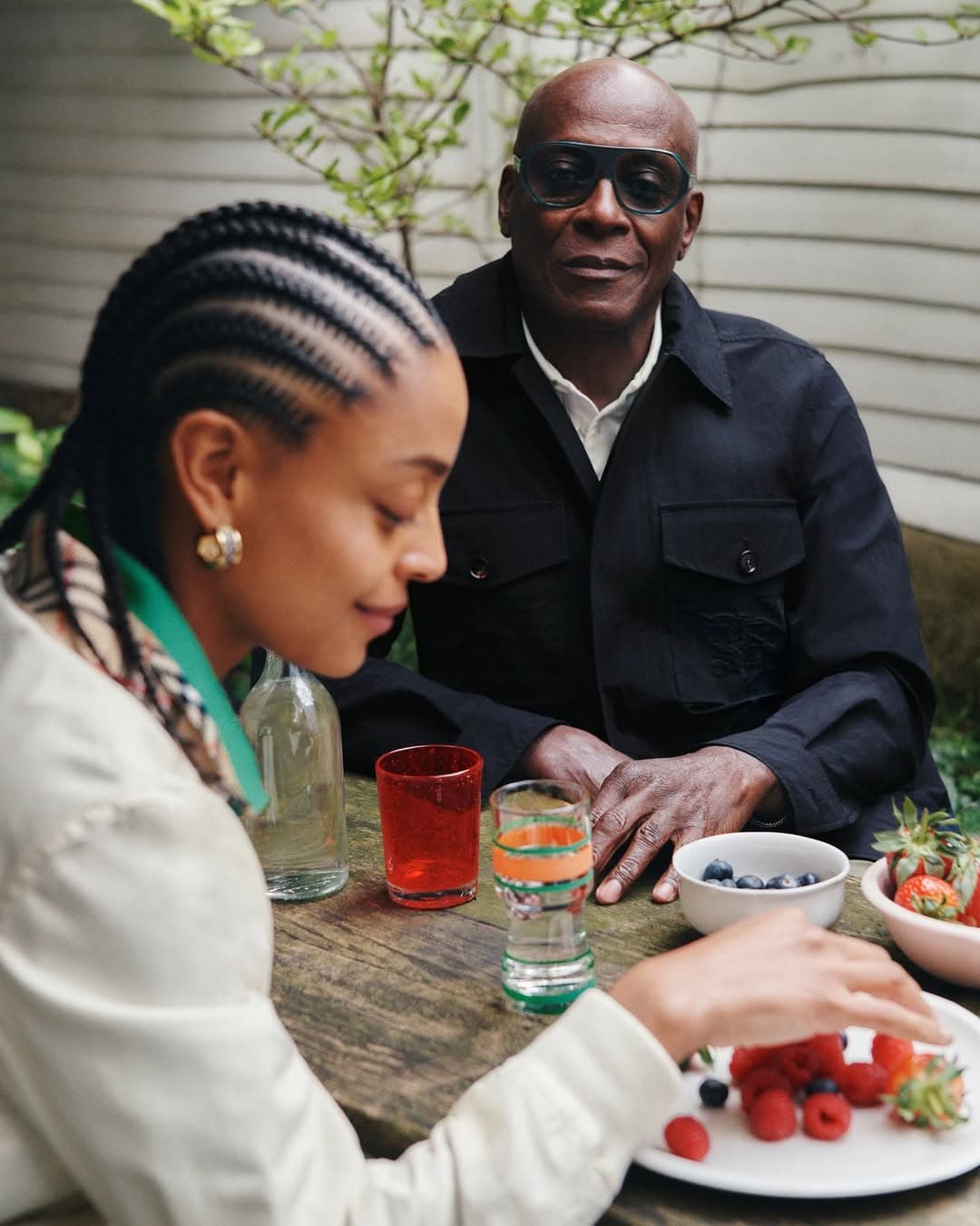 Two people at an outdoor table, one looking down, the other waiting