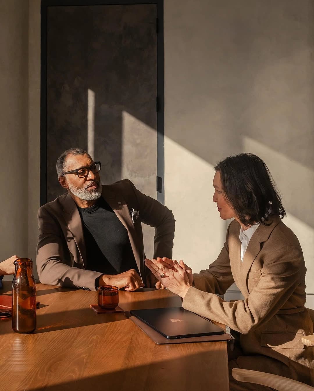 Two colleagues talking it through across a table, afternoon light on the wall